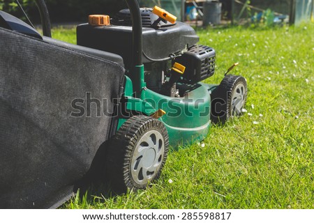 A petrol lawn mower cutting an overgrown lawn.
