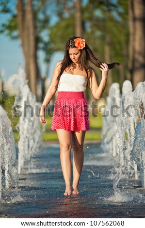 young beautiful brunette girl wearing red skirt playing at outdoor water fountain in a hot day