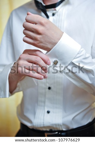 A groom putting on  cuff-links as he gets dressed in formal wear .Groom\'s suit