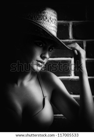 Attractive  blond model with bra and hat  standing near red brick wall .Black and white Fashion portrait of a cute blonde near a brick wall .