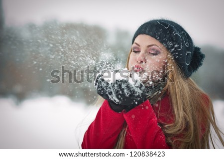 Happy girl with cap and gloves playing with snow in the winter landscape.Young woman blowing snow, winter fun