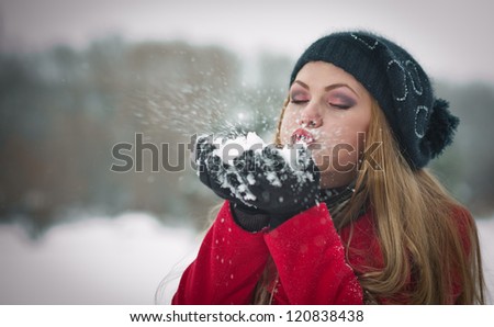 Happy girl with cap and gloves playing with snow in the winter landscape.Young woman blowing snow, winter fun