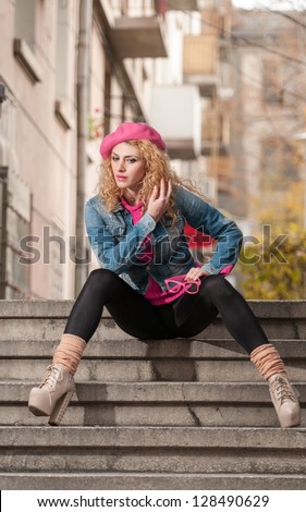 Beautiful fashion woman with pink cap sitting on stair .Young fashionable beautiful girl sitting on stair and looking around