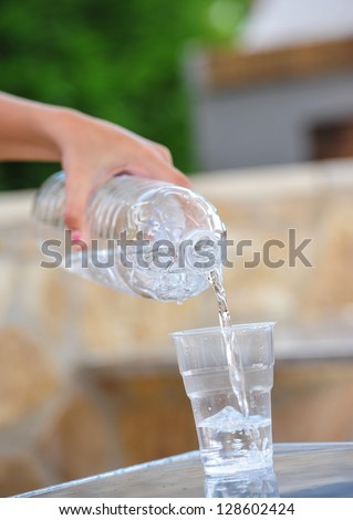 Hand pouring water on a glass.Bottle pouring water into a plastic glass.Drinking water pouring into glass outdoor.