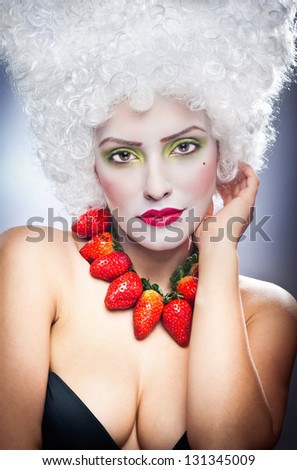 Creative makeup beauty shot of model with strawberries, artistic edit .Woman with strawberry necklace, wig and makeup professionally posing in studio.Beauty with