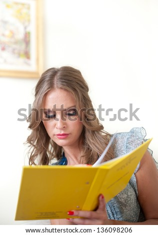 A woman reading a book and smiling as she sits on the chair.Close up of a woman reading a book in her living room .Beautiful woman reads the book lying on the white leather sofa