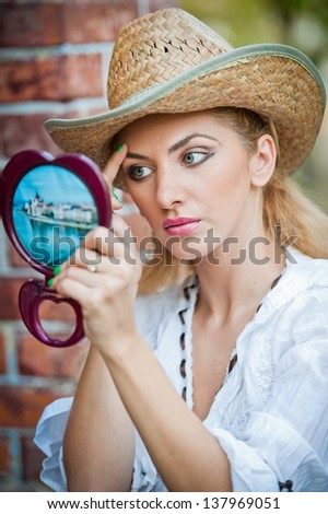 beautiful woman with straw hat and mirror .Young woman looking in cosmetic mirror .Good looking beautyfull  woman doing make-up in front of mirror.