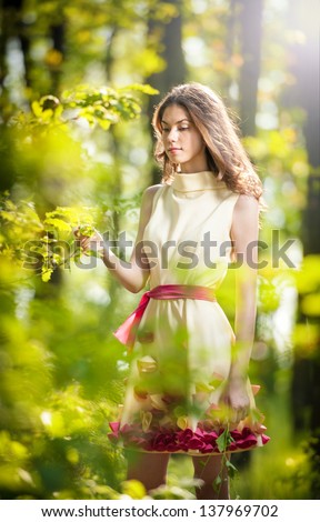 Young beautiful girl in a yellow dress in the woods .Portrait of romantic woman in fairy forest .Shot of a Stunning Teenage Model in Forest