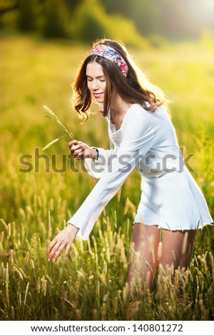 Girl with white shirt on the field at sunset.Young beautiful woman standing in wheat field .Vintage looking picture of a Young woman standing in a wheat field .Sun at early sunset in the background.