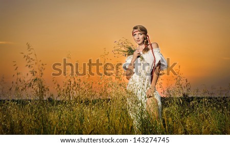Young woman standing on a wheat field with sunrise on the background.Portrait of girl in field.Romantic young woman posing outdoor.Attractive woman in white dress in yellow wheat field at sunrise.