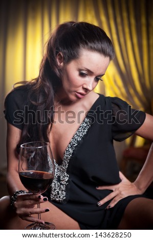 Beautiful sexy  woman with glass of wine thinking. Looking away. Portrait of a woman with long legs posing challenging  .Brunette sexy woman sitting in wood chair and drinking  in a vintage scene