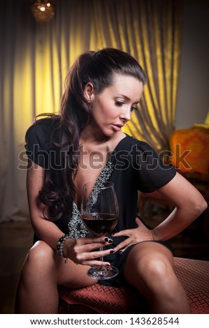 Beautiful sexy  woman with glass of wine thinking. Looking away. Portrait of a woman with long legs posing challenging  .Brunette sexy woman sitting in wood chair and drinking  in a vintage scene