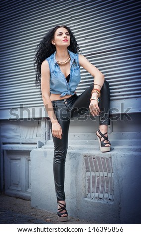 Attractive woman in black leather pants and shirt posing on the street.Long-haired beauty with a gorgeous body in black leather pants in the city