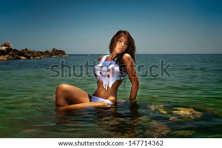 fashion portrait of young sexy brunette girl in bikini and wet t-shirt at the beach.Sensual attractive woman in water wearing bikini and nice tits. Woman with perfect body relaxing on the beach.