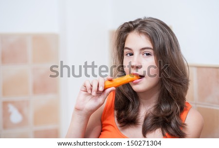 Pretty teen girl eating carrot, indoor.Beautiful teenage girl biting from a carrot. Picture of beautiful teenage biting from  a carrot