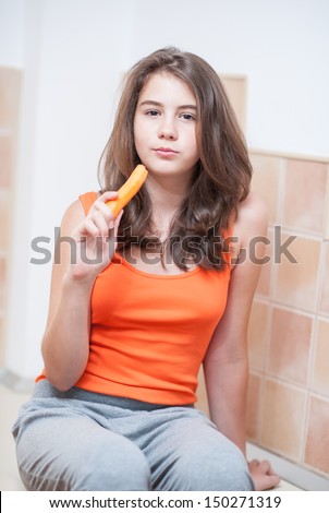 Pretty teen girl eating carrot, indoor.Beautiful teenage girl biting from a carrot. Picture of beautiful teenage biting from  a carrot