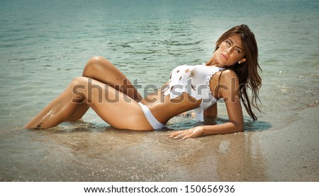 portrait of young sexy brunette girl in white bikini and wet t-shirt at the beach.Sensual attractive woman in water wearing bikini and long legs . Woman with perfect body relaxing on the beach.