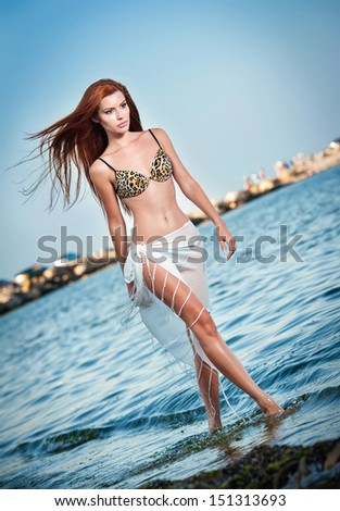 fashion portrait of young sexy brown girl in swimsuit walking on the beach.Sensual attractive woman in water wearing long legs. Woman with perfect body walking and relaxing on the beach