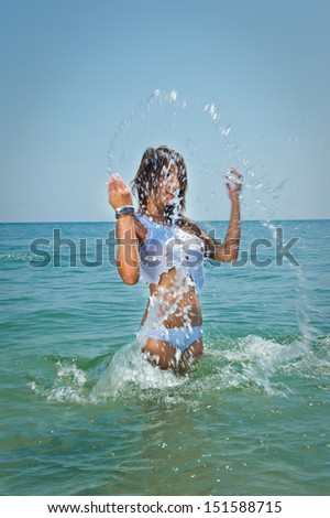 young sexy brunette girl in white bikini and wet t-shirt playing in the water.Sensual attractive woman in water wearing bikini and long legs .Woman with perfect body relaxing and playing on the beach.