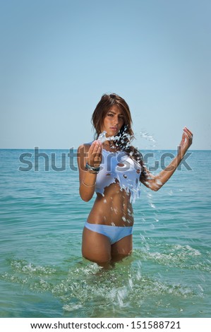 young sexy brunette girl in white bikini and wet t-shirt playing in the water.Sensual attractive woman in water wearing bikini and long legs .Woman with perfect body relaxing and playing on the beach.