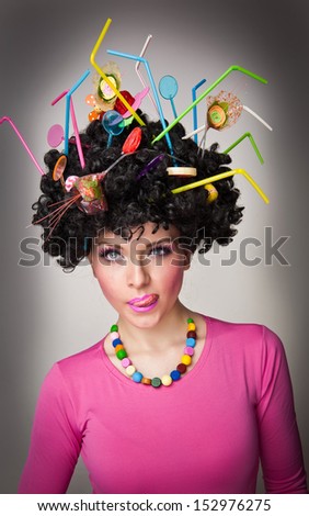 Portrait of a beautiful female model on white background with lollipops in the hair.Glamorous girl with pink blouse wearing  lollipop and straw colored in hair