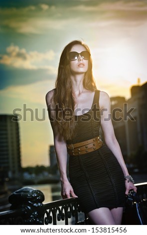Fashion model on the street with sunglasses and short black dress.Fashionable girl with long legs posing on street.High fashion urban portrait of young, slim, beautiful model