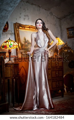 Young beautiful luxurious woman in long elegant dress. Beautiful young woman in a luxurious classic interior. Seductive brunette woman in luxury manor, vintage style