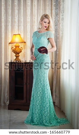 Young beautiful luxurious woman in long elegant dress. Beautiful young blonde woman in turquoise dress with curtains in background. Seductive blonde woman in lace dress in luxury manor, vintage style