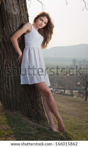 Pretty young woman posing laying on a tree. Very attractive blonde girl with white short outdoor on a hill. Romantic young woman posing outdoor in the field