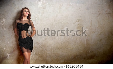 Charming young brunette woman in transparent lace black dress leaning against an old wall. Sexy gorgeous young woman near old wall. Full length portrait of a sensual woman with long hair posing