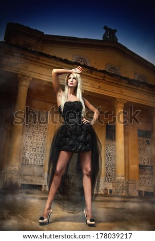 Beautiful woman in black dress posing outdoor. Sexy woman in stylish retro scene. Elegant woman in front of a castle. Portrait of woman in black elegant dress standing in front of an old building