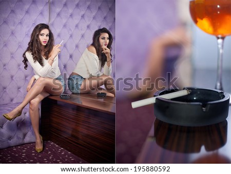 Beautiful brunette girl in denim shorts and white blouse posing on lilac textured background smoking. Young sensual woman siting alone in a modern night club with a cigarette in ashtray and glass.