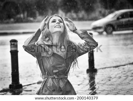 Beautiful woman wearing a coat posing in the rain. Happy long hair girl enjoying the rain drops in the park, outdoor shot. Attractive female relaxing in a rainy day. Black and white photo