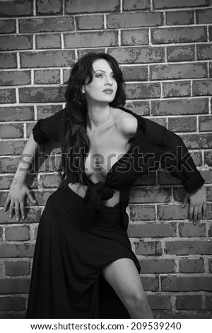 Charming young brunette woman in black near the brick wall. Sexy gorgeous young woman with low cut blouse. Portrait of a provocative woman with long hair laying against a red brick wall