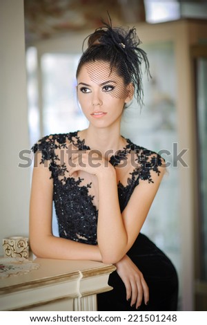 Beautiful brunette lady in elegant black lace dress posing in a vintage scene. Young sensual fashionable woman with creative hairstyle indoor. Attractive slim girl indoor shot in luxurious scenery