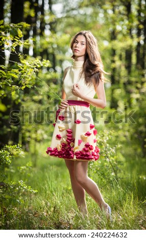 Young beautiful girl in a yellow dress in the woods. Portrait of romantic woman in fairy forest.  Stunning fashionable teenage model in summer meadow, outdoor shot. Cute brunette long hair female.