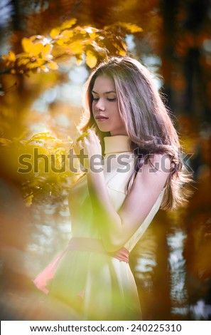 Young beautiful girl in a yellow dress in the woods. Portrait of romantic woman in fairy forest.  Stunning fashionable teenage model in autumnal meadow, outdoor shot. Cute brunette long hair female.