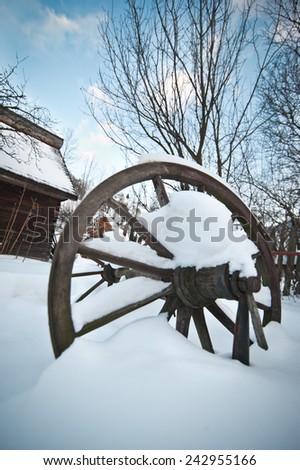 Old wooden cottage and wooden Romanian wheel covered by snow. Cold winter day at countryside. Traditional Carpathian mountains village scenery, Romania. Small cabin covered by snow