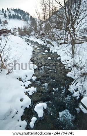 View of frozen river countryside. Brook in snowy landscape. Romanian small river in winter scenery, Romania, Moeciu. Wild brook in winter season.