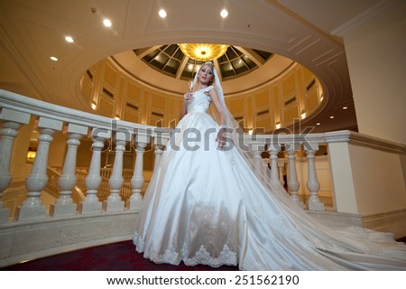 Young beautiful luxurious woman in wedding dress posing in luxurious interior. Bride with huge wedding dress in majestic manor. Seductive blonde bride with gorgeous gown and long dally posing