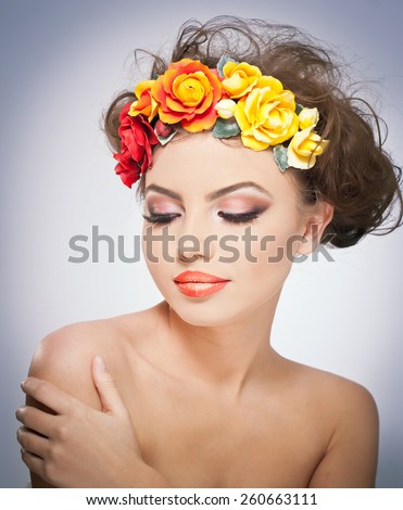 Portrait of beautiful girl in studio with red and yellow roses in her hair and naked shoulders. Sexy young woman with professional makeup and bright flowers. Creative hairstyle and makeup, studio shot