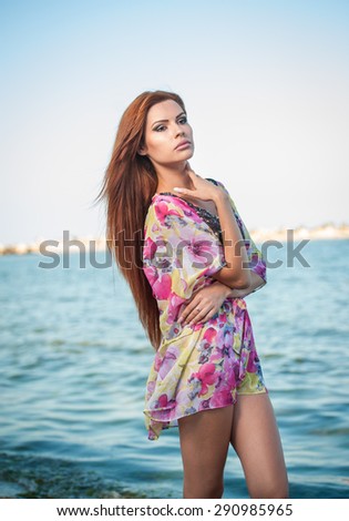 Young sexy red hair girl in multicolored blouse posing on the beach. Sensual attractive woman with long hair, summer shot at sea shore. Perfect body female, holiday concept turquoise water backgroud