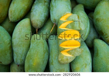 Slice of fresh green mango for sale in the market. many yellow ripe mango on background. Top view. Close up.