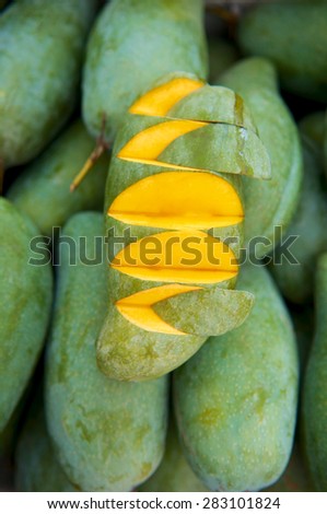 Slice fresh mango for sale in the market. many yellow ripe mango on background. Top view, vertical. Close up.