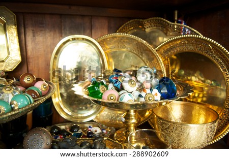Thai antique gold accessory set for sale at old market. Close up of colorful gem decorations and brass bowl tray. Thailand ancient handicrafts shop. Vintage and retro store for collector.