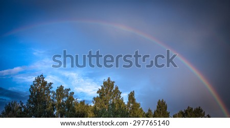 Beautiful colorful rainbow in the rain against the blue sky and dark clouds, weather phenomenon, purple, blue, green, yellow, orange, summer, autumn