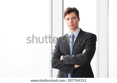 Portrait of handsome businessman standing near windows in office