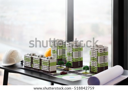 Model of apartment house, blueprint and hardhat on table in office
