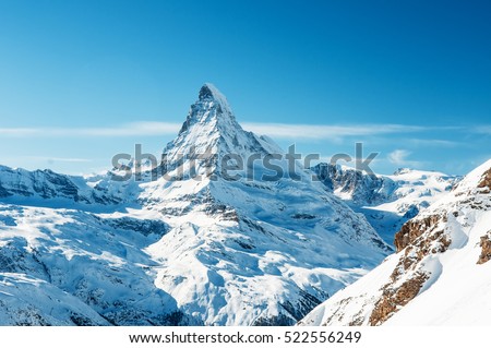 Scenic view on snowy Matterhorn peak in sunny day with blue sky and some clouds in background, Switzerland.