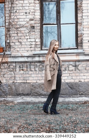 Portrait of young cute woman in autumn coat on the background of houses. Fashion photo. Hair of girl is blowing in the wind